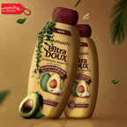 Two bottles of Garnier Ultra Doux shampoo with avocadoes on a brown background