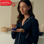Woman in a dark blue robe holding a blue container with a beige background and promotional text.
